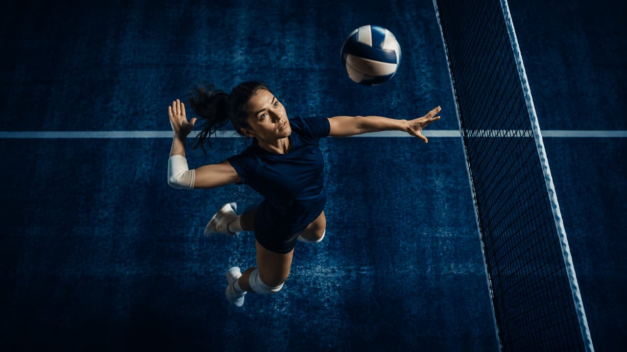 Volleyball player leaping to serve, seen from above on a floodlit court